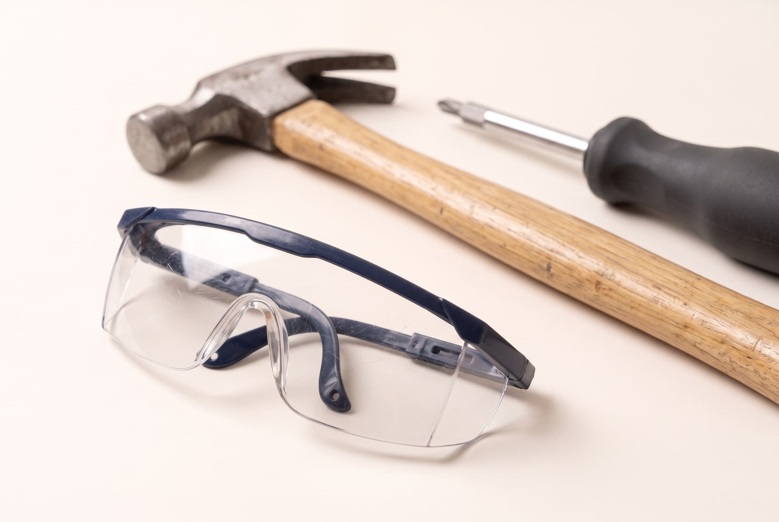 Child-sized safety glasses resting on the ground, with the hammer's wooden handle and the screwdriver's grip behind them.
